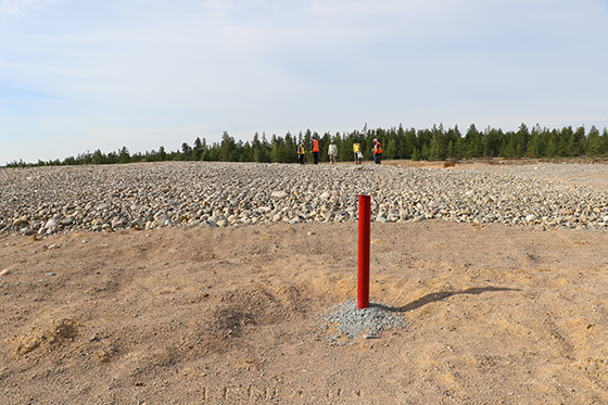 Un tube rouge sort de la terre devant un champ de gravier qui couvre l'enfouissement complété.