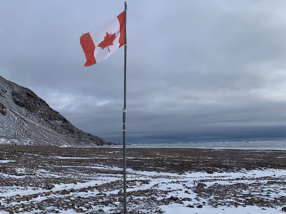 Drapeau canadien sur un mât dans un paysage gelé.