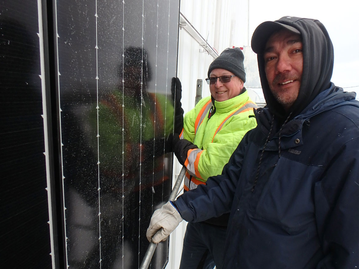 Mr. Schneider and Christian Christiensen in front of a solar panel turning and smiling at the camera.