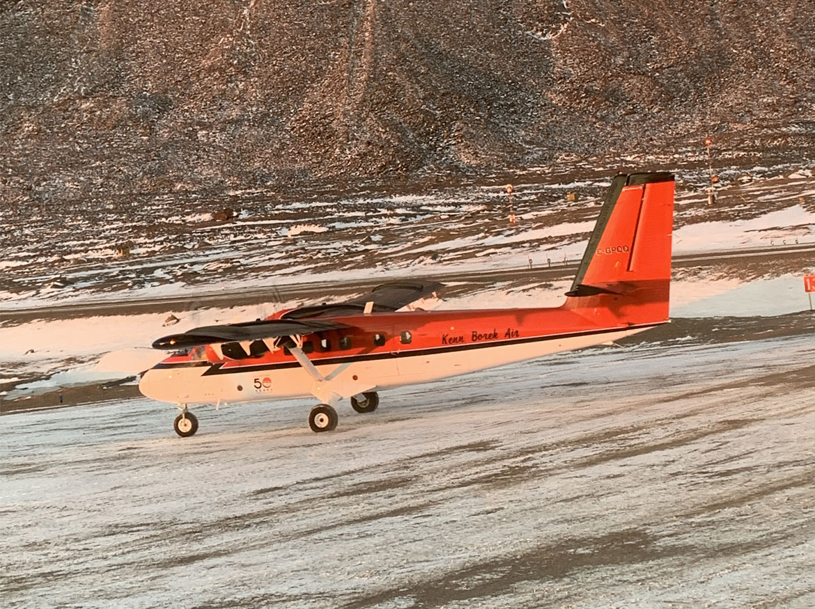 Small freight red and white plane on the ice with a mountain in the background.