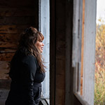 Marilyn debout devant la fenêtre de la cabane de ses grands-parents regarde dehors.