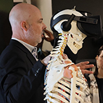 Boucher standing behind a skeleton model wearing a virtual reality headset.