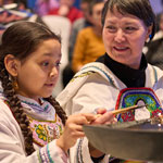 A young Inuk girl lighting the Qulliq lamp with an Elder.