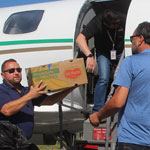Three people loading a plane with boxes of food.