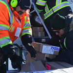 Trois travailleurs de Harvest Manitoba chargent un avion de nourriture.