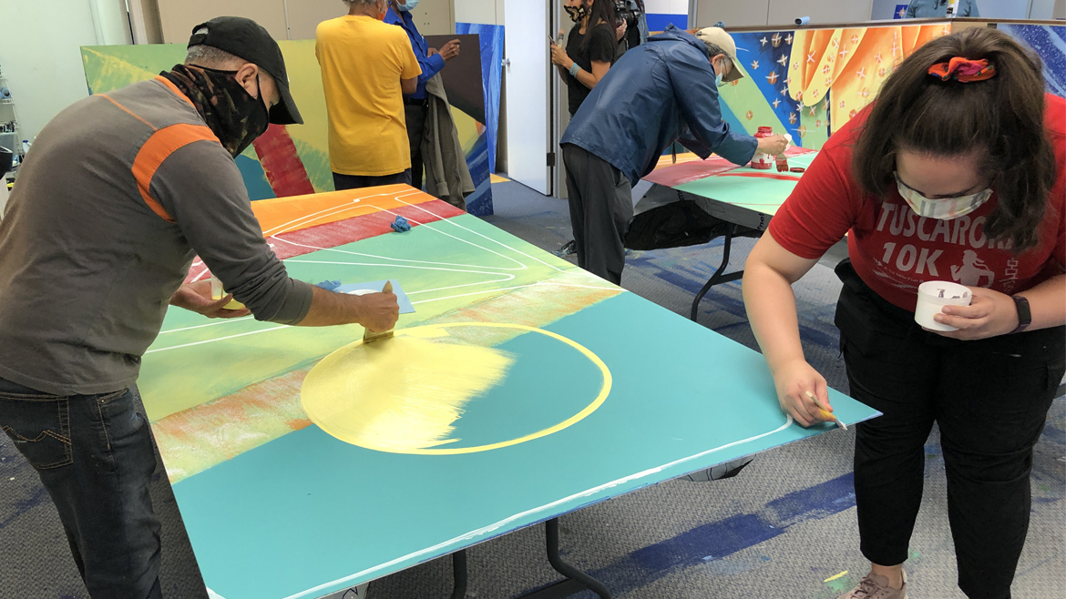 Volunteers wearing surgical face masks painting a mural panel