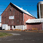 A silo and a brown barn with a sign for Mādahòkì Farm.