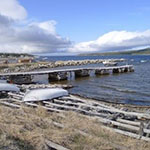 Two small boats on the shore beside a dock, with the town of Makkovik in the background.