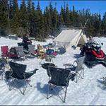 A tent and chairs set up around a firepit in the snow.