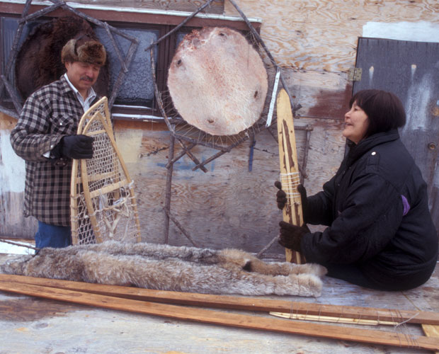 Two northern community members with hunting equipment and snowshoes.