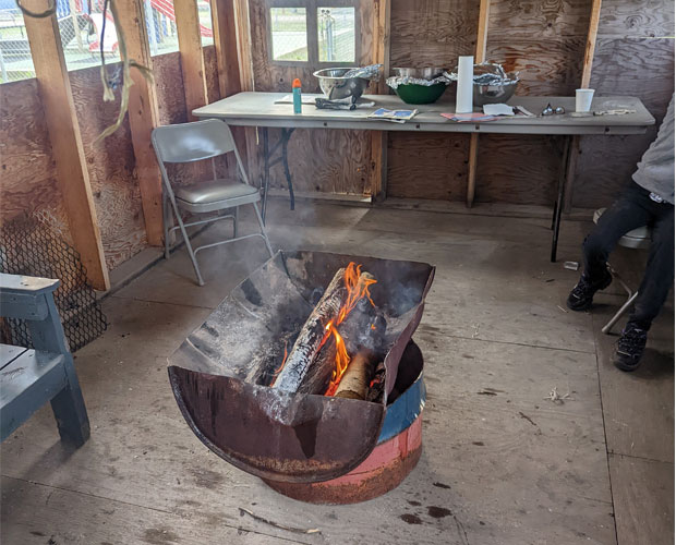 Interior of a smokehouse in a northern community with a wood-fuelled smoker, food preparation area, and smoked fish hanging overhead.