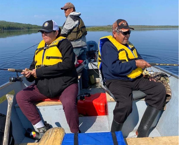 Three people on a boat wearing lifejackets and holding fishing poles.