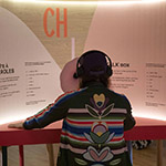 Xavier est assis devant une exposition intitulée « boîte à parole » au Musée des Abénakis.