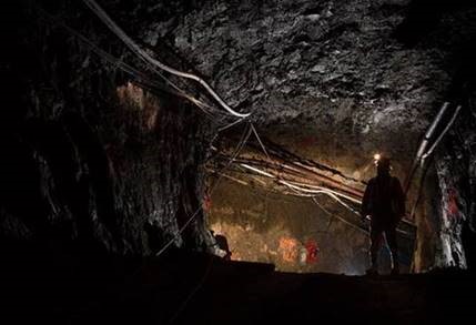 Photo de la silhouette d’une personne portant un équipement de protection personnelle dans un tunnel d’une mine souterraine. Le tunnel est creusé dans la roche, et des fils et des tuyaux se trouvent dans la section supérieure.