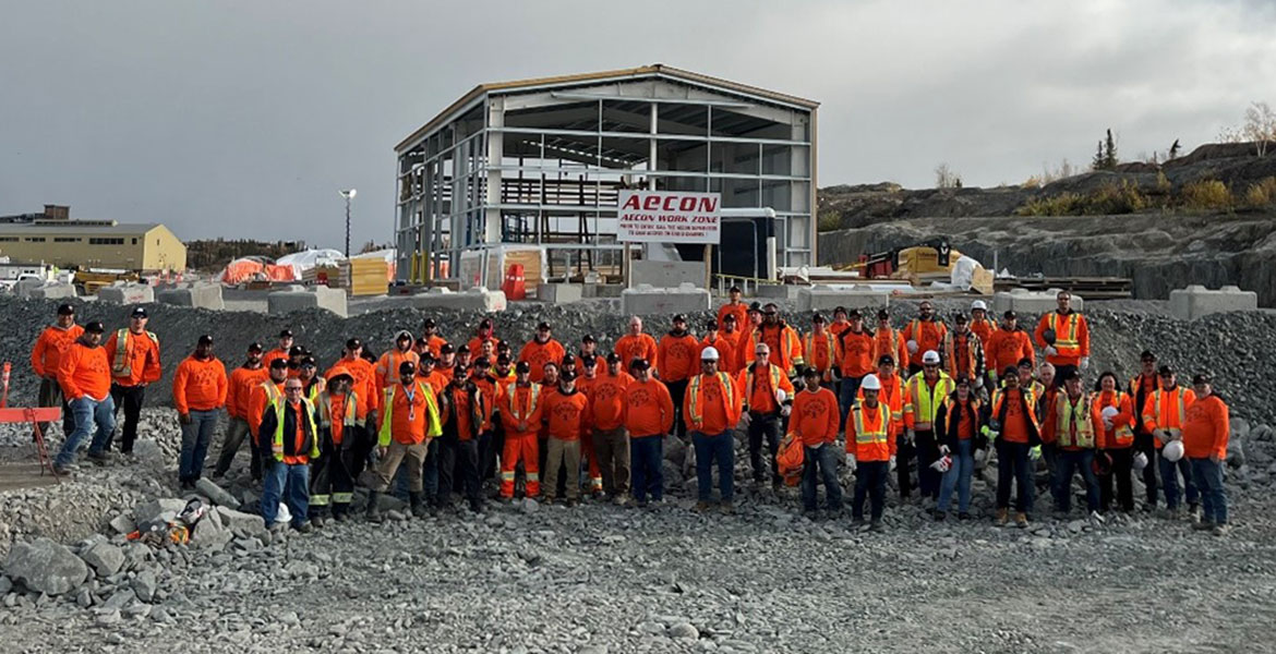 Un groupe de travailleurs de la construction portant des gilets de sécurité se tient devant le cadre du bâtiment.