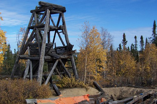 Un chevalement de bois délabré au-dessus d'un puits ouvert entouré d'arbres.