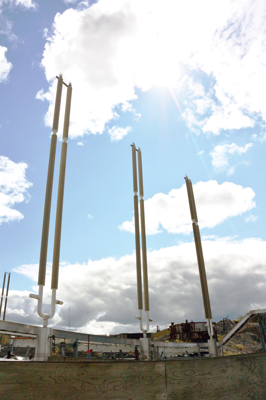 Thermosyphons, which are long vertical pipes sticking out of the ground, with an old building visible in the background.
