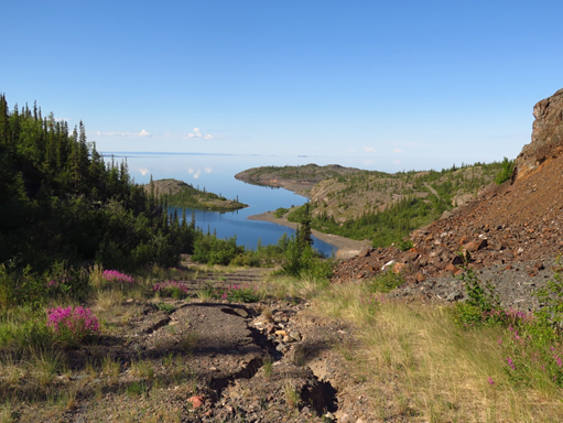 Une route de terre en mauvais état mène au site principal de Port Radium, en avant-plan du Grand lac de l’Ours.