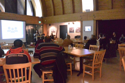 The image shows CanNorth consultant Stacey Fernandes presenting on the results of the HHERA. Yellowknife residents look on from tables in the Museum Café. 