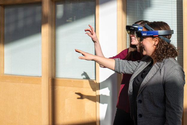 Two women wearing virtual reality goggles are shown reaching out toward what they can see within the experience.