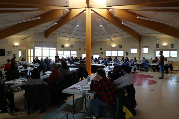 This picture shows a room full of people sitting at tables in a meeting.